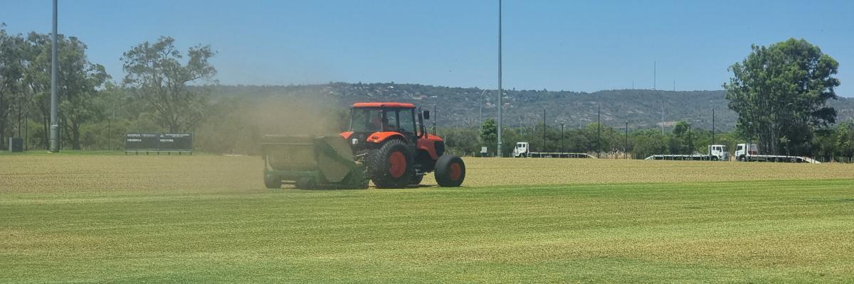 Large tractor towing verti-mower on sports ground at Mills Park