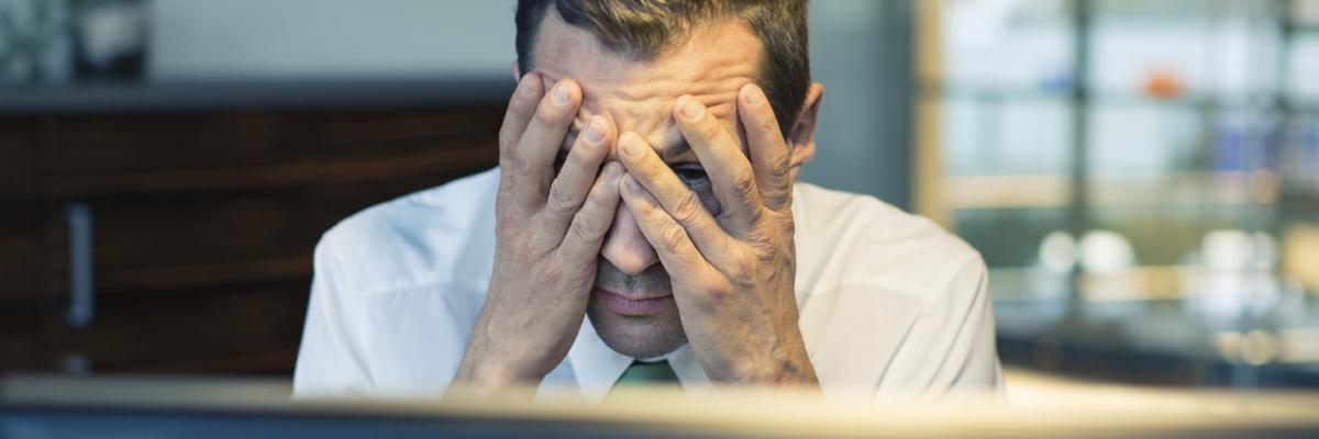 A man with his head in his hands, sitting in front of a computer screen.