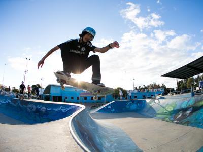 A man in the air on a skateboard at a skatepark going over the lip from one section to the other