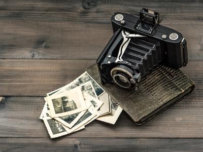 A collection of black and white photographs on the floor, next to an old-fashioned camera