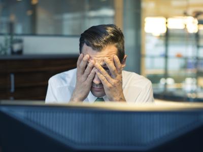 A man with his head in his hands, sitting in front of a computer screen.